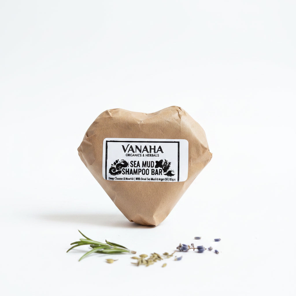 A heart-shaped brown paper-wrapped shampoo bar with a white label reading 'VANAHA ORGANICS & HERBALS SEA MUD SHAMPOO BAR,' placed on a beige woven sack with a patterned red rug in the background.