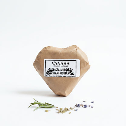 A heart-shaped brown paper-wrapped shampoo bar with a white label reading 'VANAHA ORGANICS & HERBALS SEA MUD SHAMPOO BAR,' placed on a beige woven sack with a patterned red rug in the background.